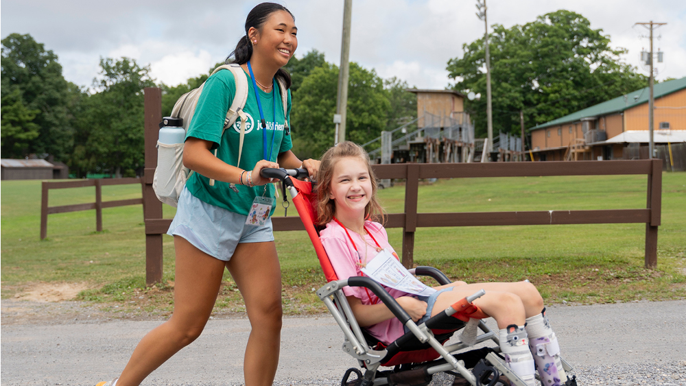 A volunteer pushes a girl in her wheelchair as they both smile for the camera
