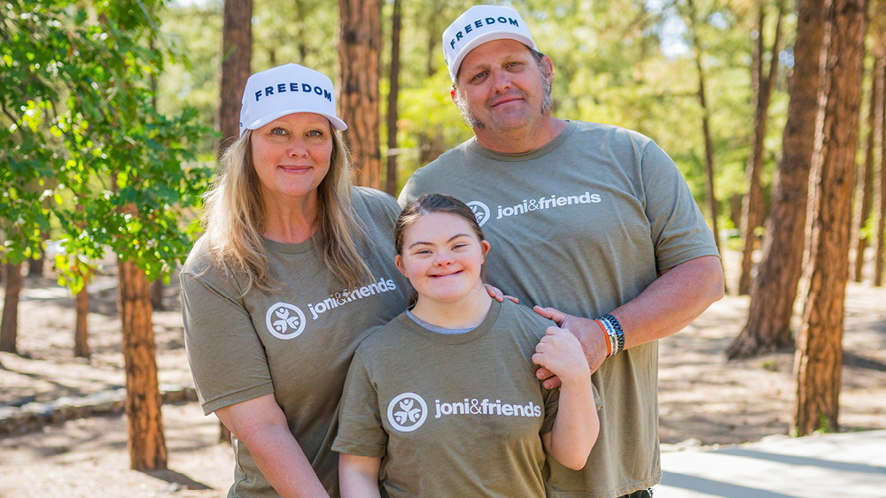 A mom, a dad, and their daughter smile and pose for the camera outdoors.
