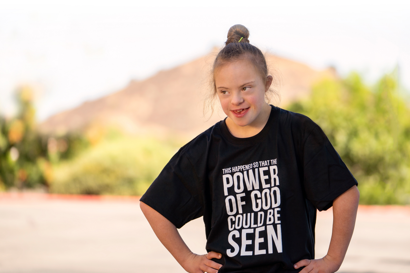 Sarah Amick poses outdoors, wearing a shirt that reads, “This happened so that the power of God could be seen.