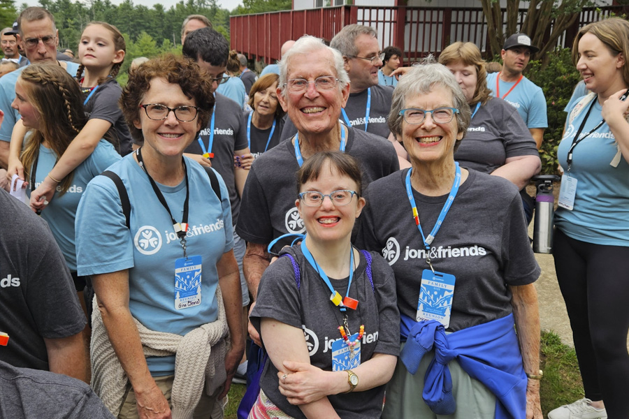 Cherry and Ron with their daughter Jenny, who has Down syndrome, standing with another woman. They are smiling and posing for a group photo with other people in the background.