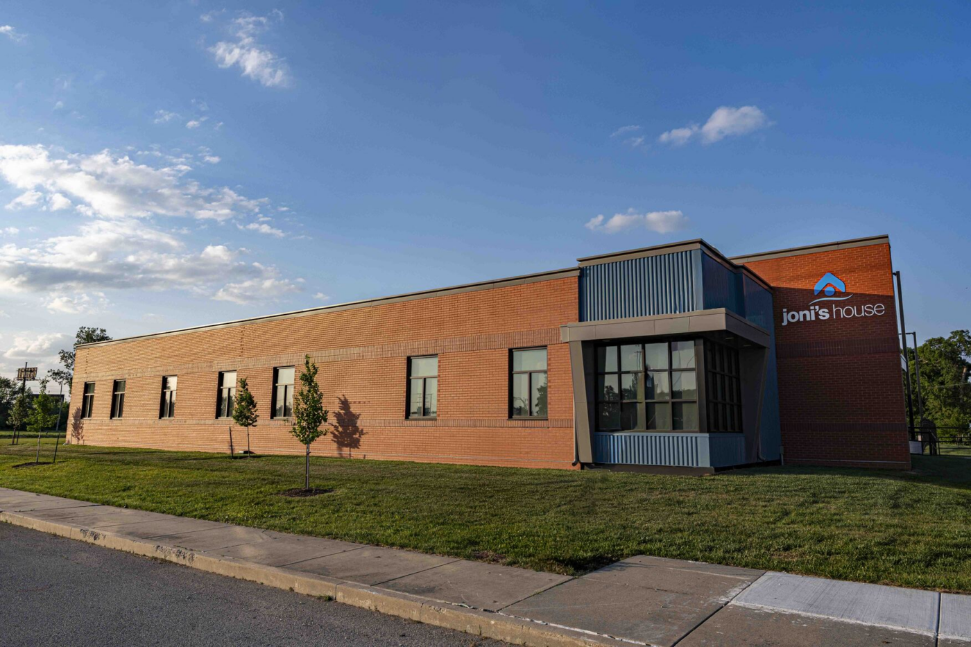 Exterior of a brick office building and a "Joni's House" sign beneath a clear blue sky.