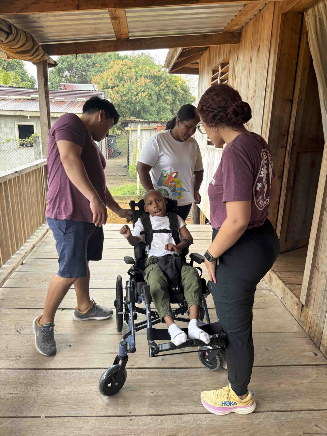 A child in a wheelchair sits while three adults adjust the wheelchair and talk with him.