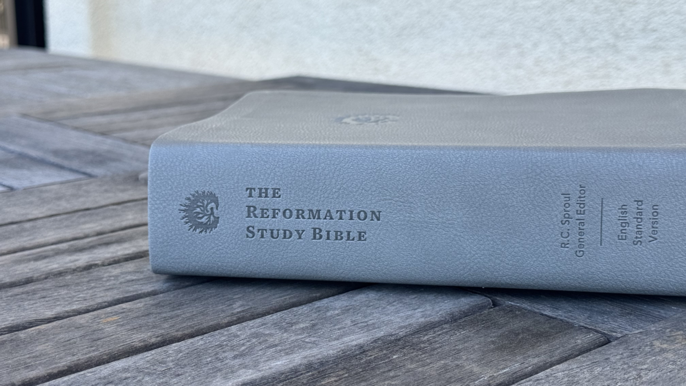 A closed leatherbound Reformation Study Bible resting on a weathered wooden table, with its title visible along the spine.
