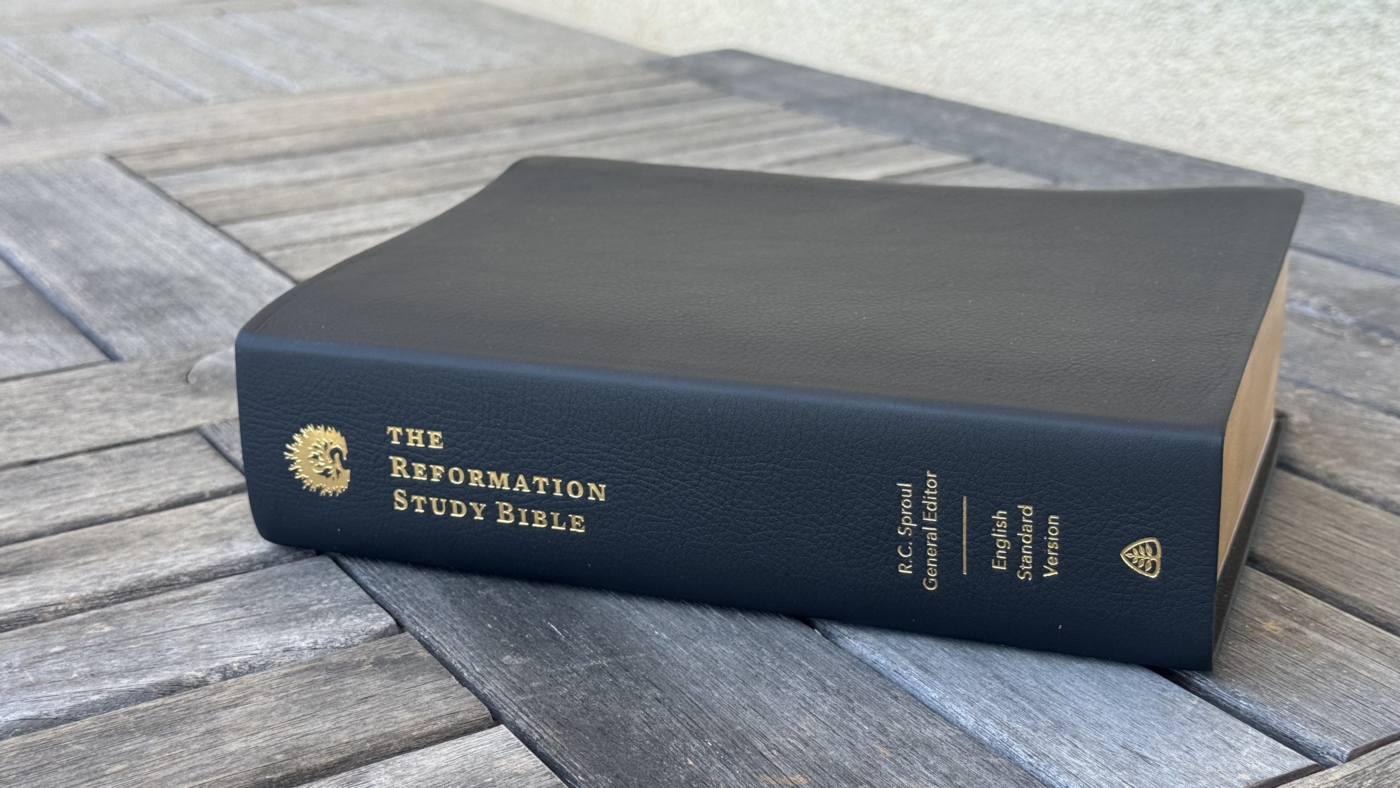 A closed leatherbound Reformation Study Bible resting on a weathered wooden table, with its title visible along the spine.
