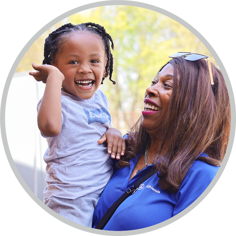 A woman carries a boy who is smiling and looking at the camera.