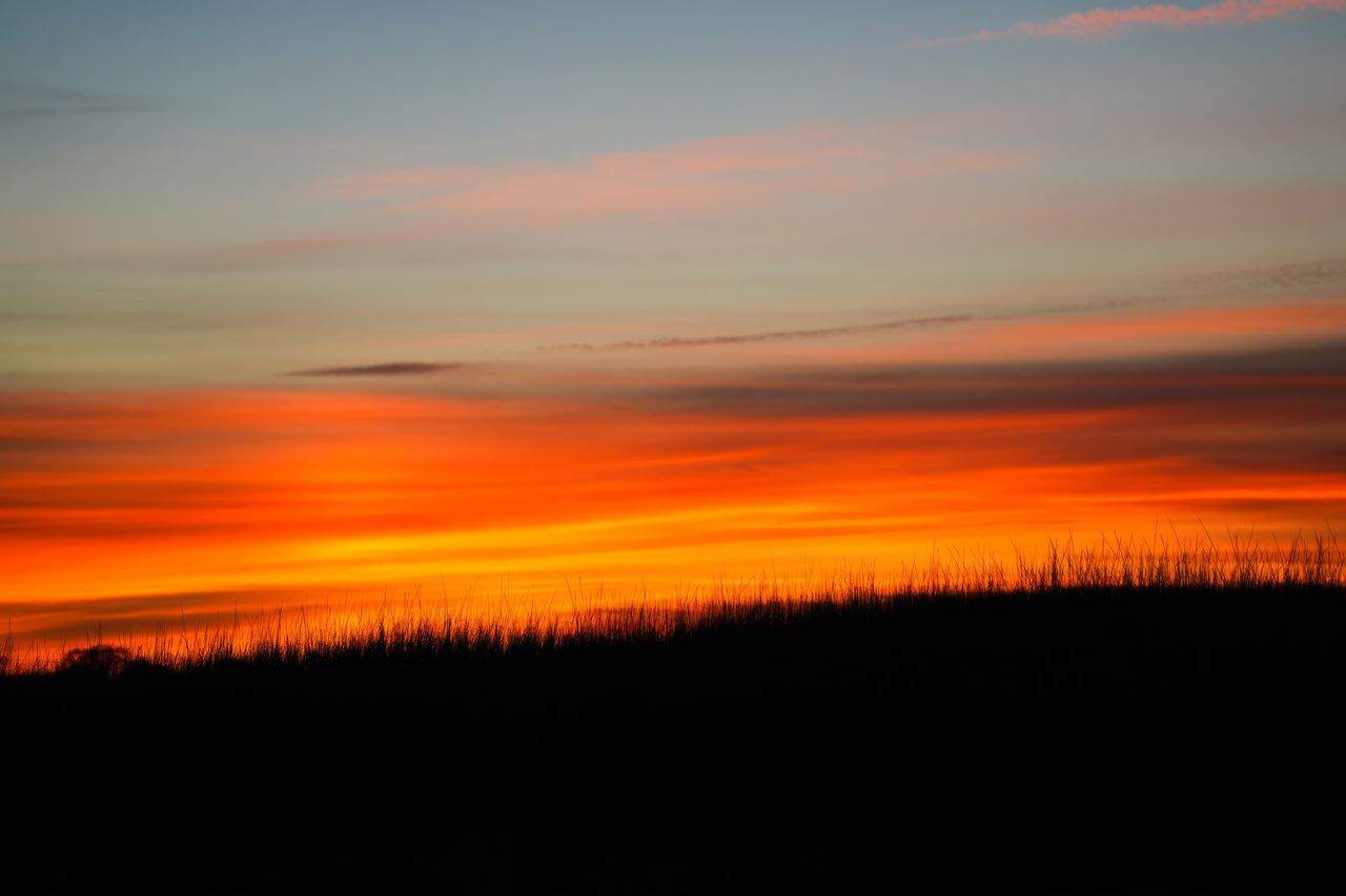 A vibrant sunset with fiery orange and red hues over a silhouetted landscape.