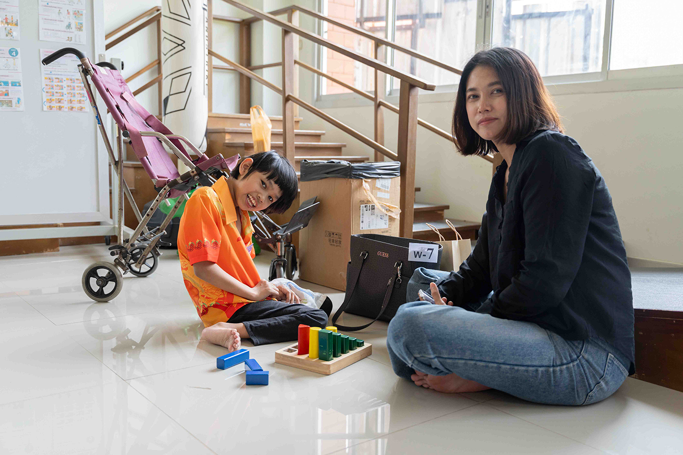 Nada, a young girl with cerebral palsy, sits on the floor with her mom, Mim, in front of her; they both look at the camera.