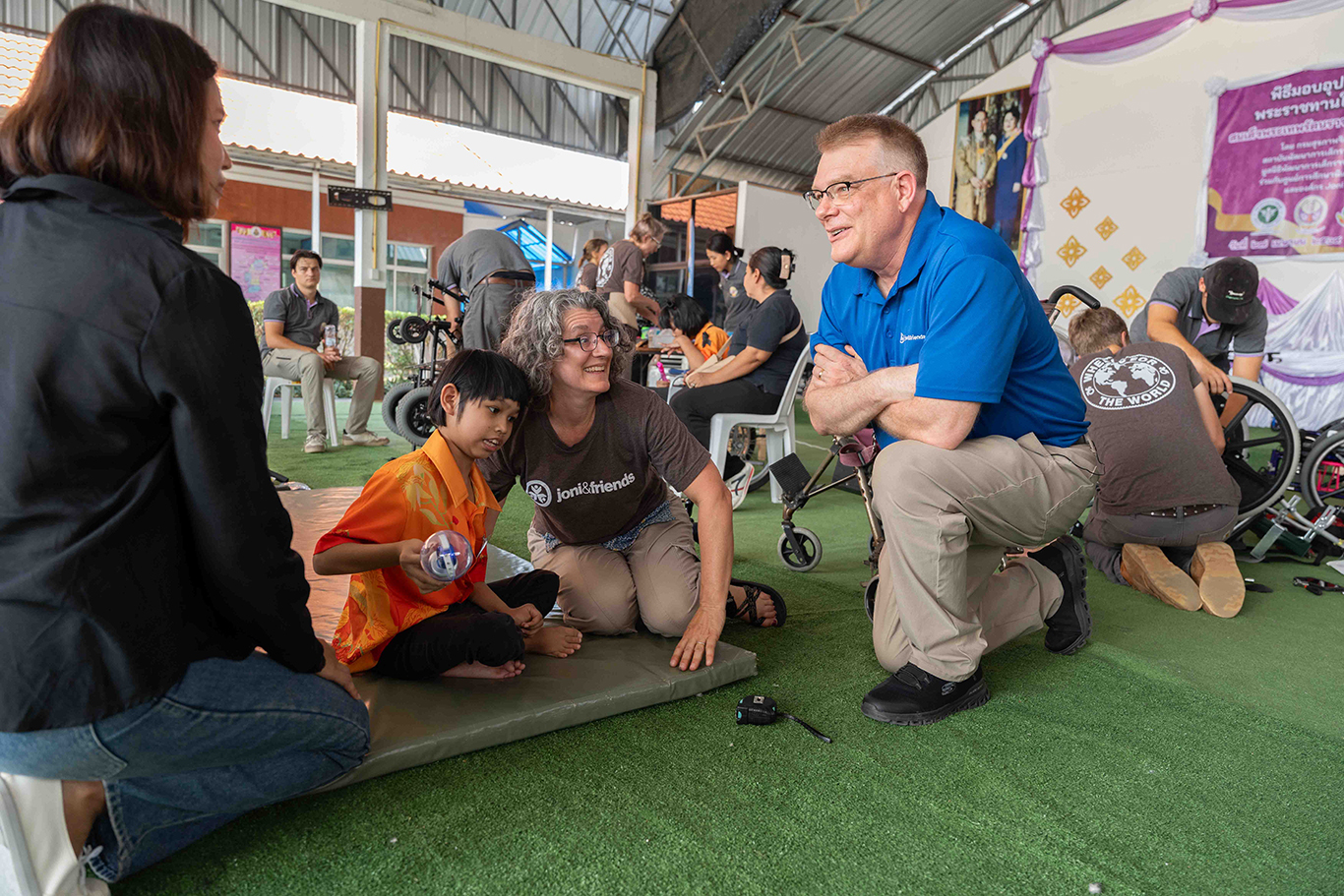 Shawn Thornton looks at and talks to Mim, Nada's mom, while Nada, a young girl with cerebral palsy, sits on a mat with a Joni and Friends volunteer next to her.