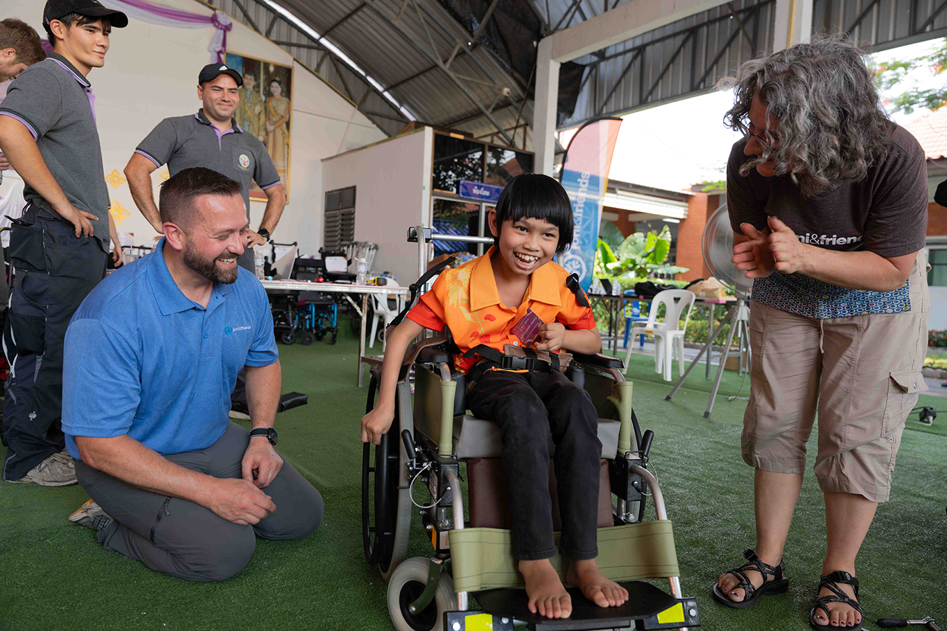Nada, a girl from Thailand, uses her new wheelchair while four people smile and celebrate with her.