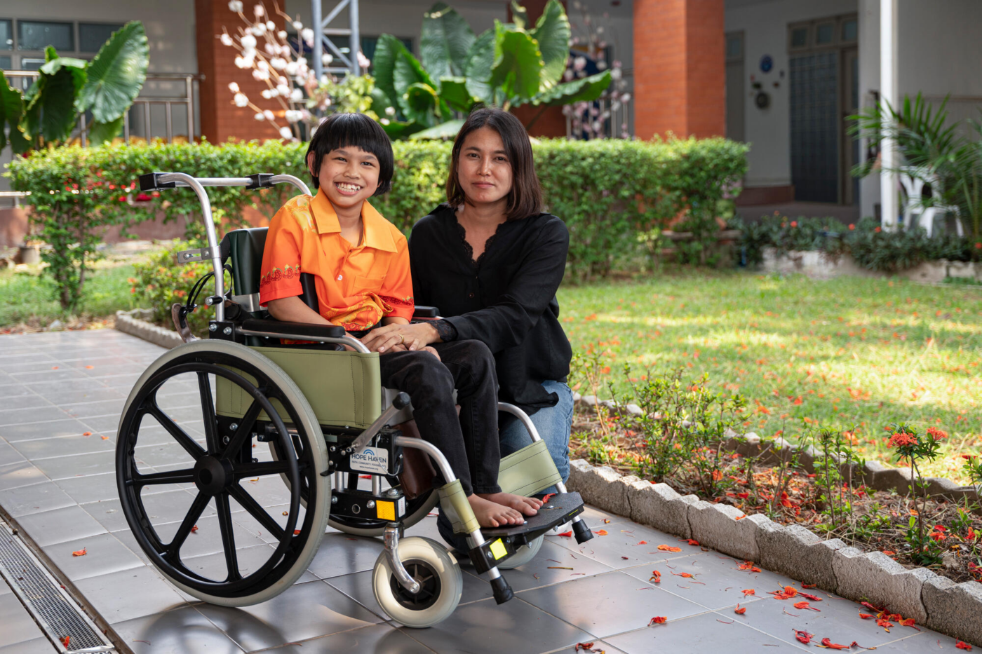 Nada, a young girl with cerebral palsy, is sitting in her new wheelchair next to her mom, Mim