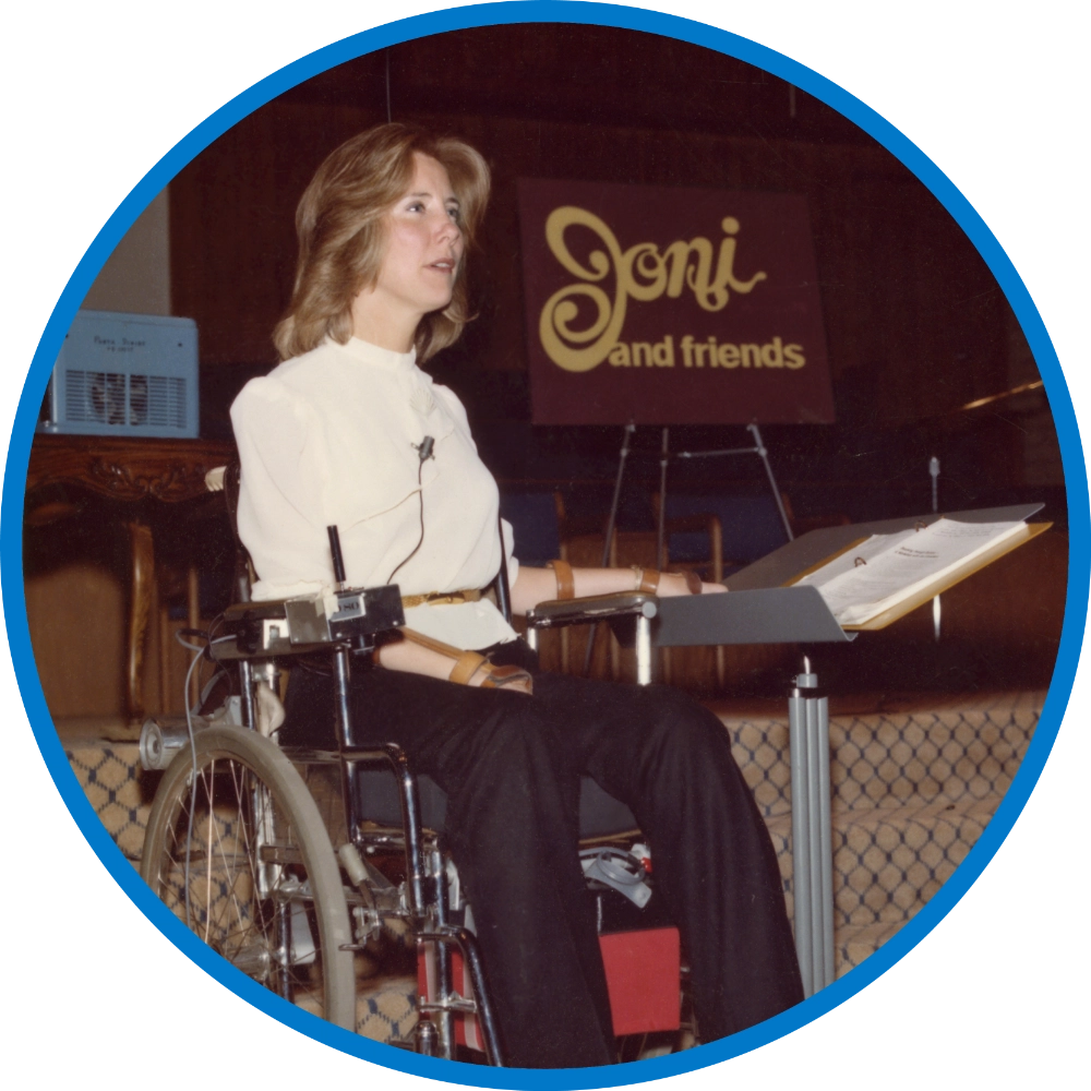 A photo of a younger Joni in front of the retro Joni and Friends logo