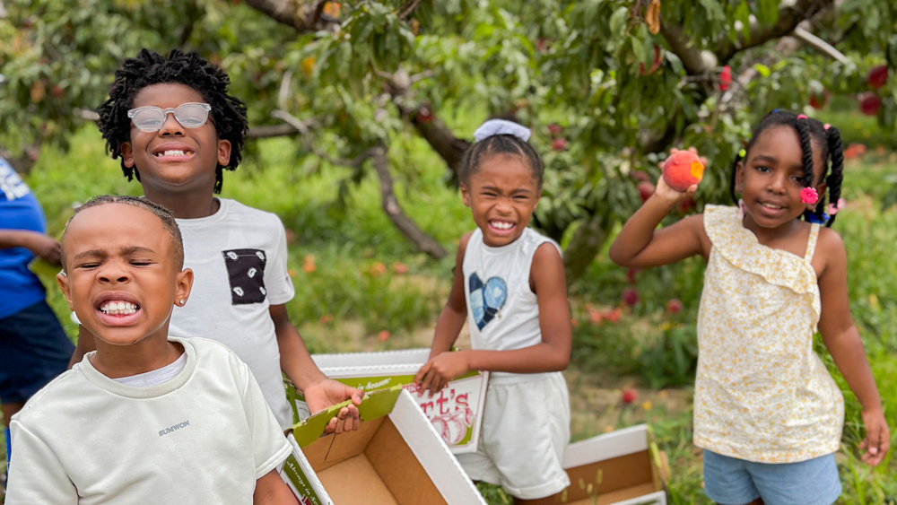 Children picking peaches smile for the camera