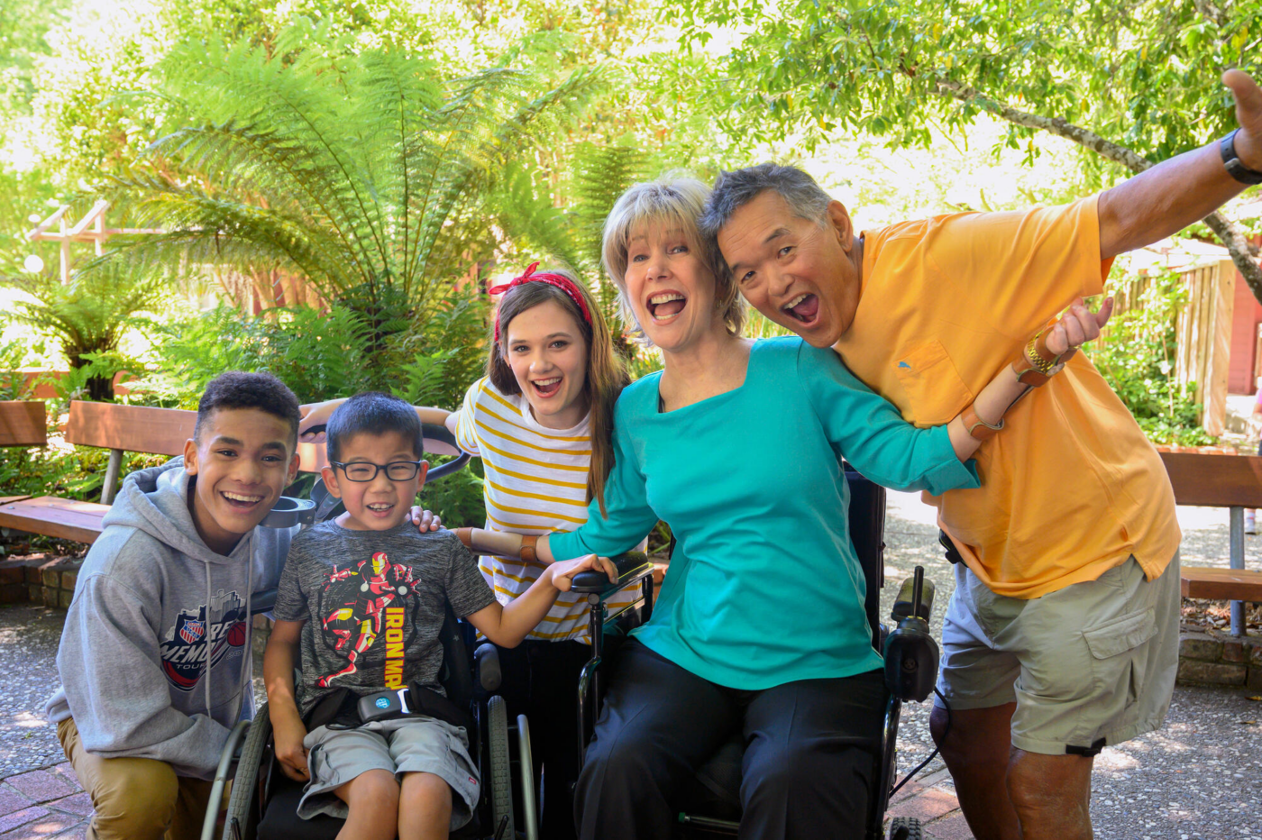 Joni and Ken pose with a little girl and a little boy in a wheelchair, all smiling happily at the camera.