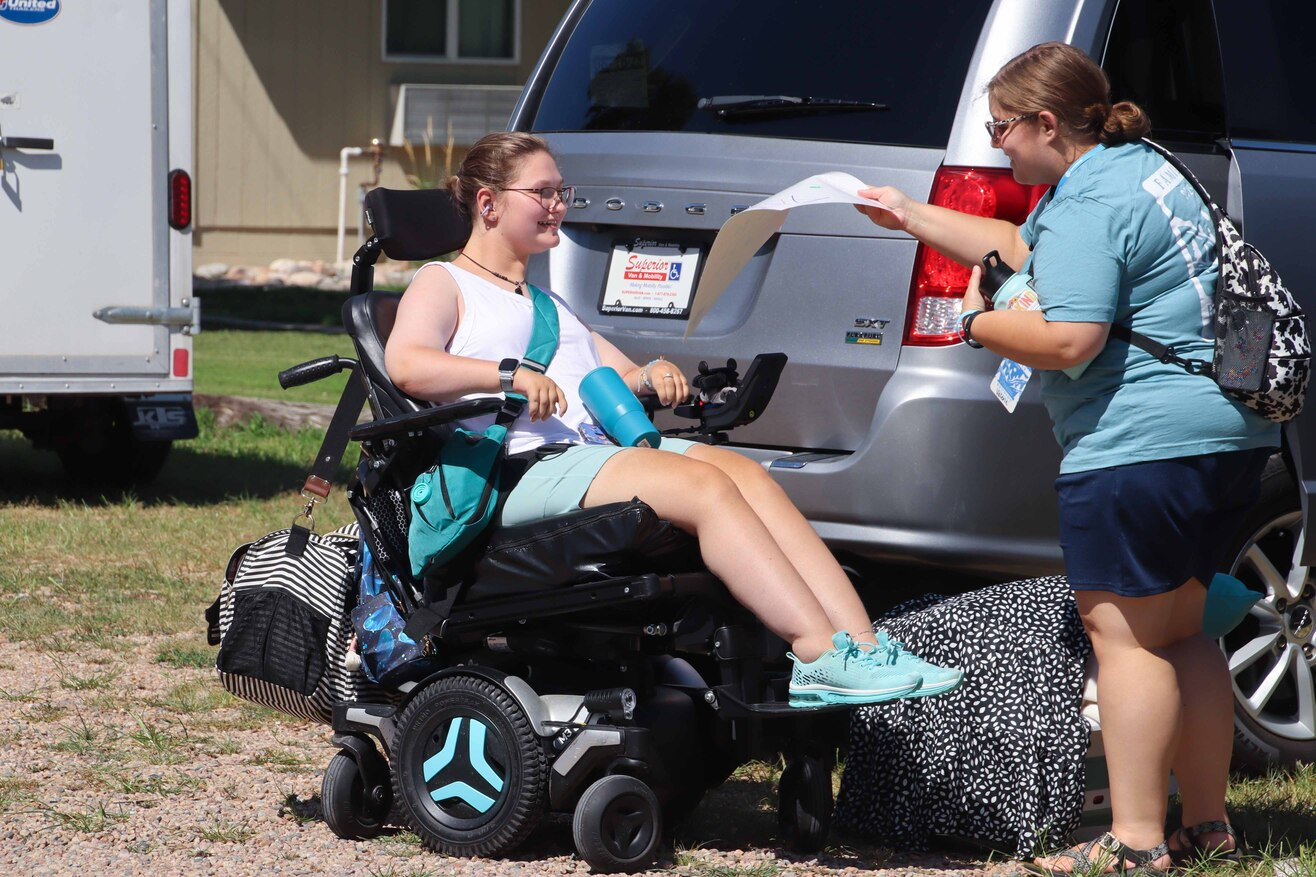 Abi smiles in her wheelchair as a volunteer hands her a piece of paper.