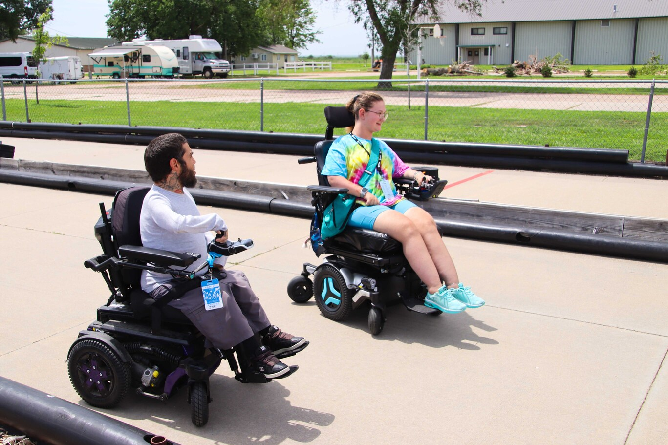 Abi drives her power wheelchair as she talks with another man in a power wheelchair.