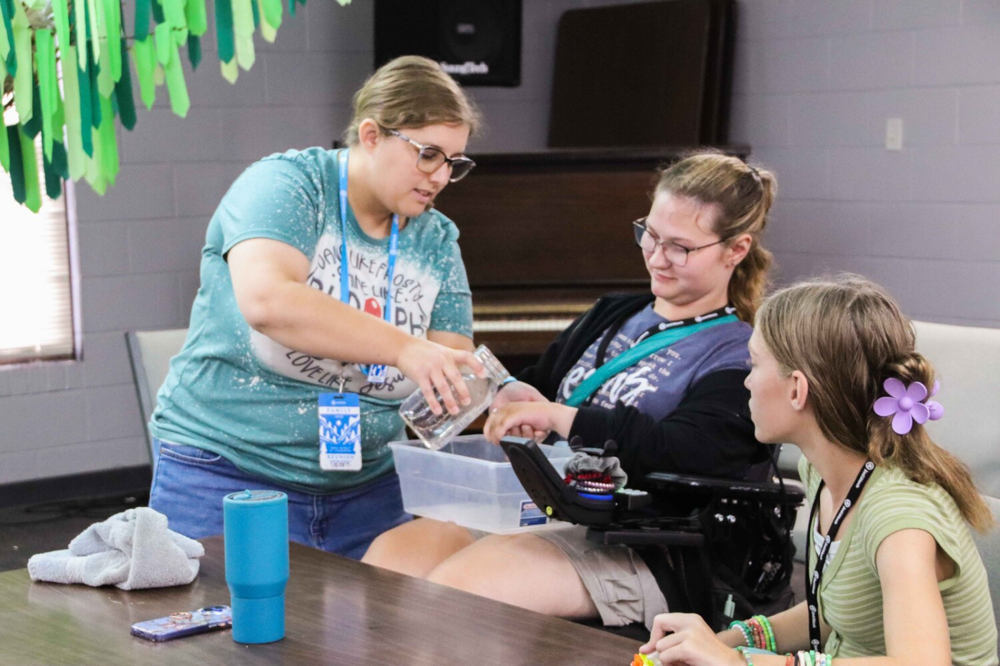 Abi looks at her hand as a volunteer pours water over it, while another girl watches.