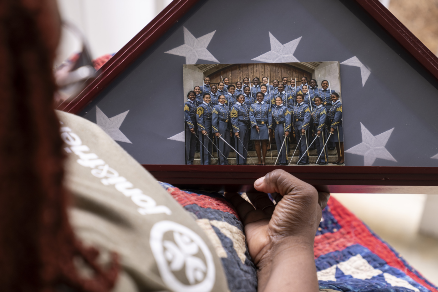 Natacha holding a triangular framed photo of a large group of soldiers in blue dress uniforms with swords.
