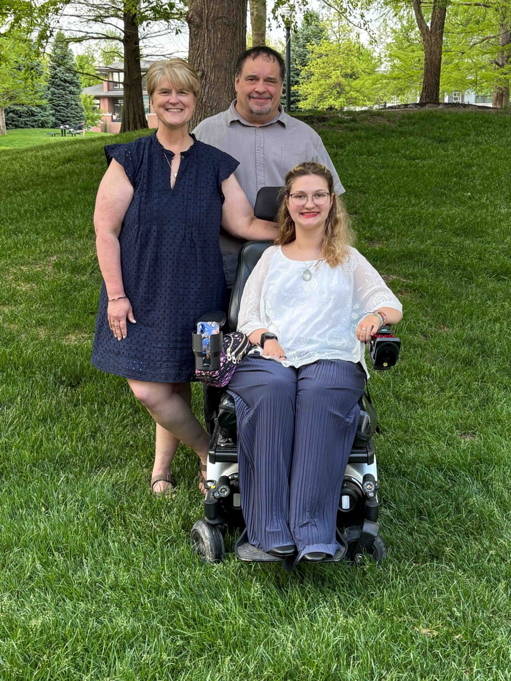 Outdoor family photo of Erica and Kevin with their daughter Abi, who is seated in her wheelchair.