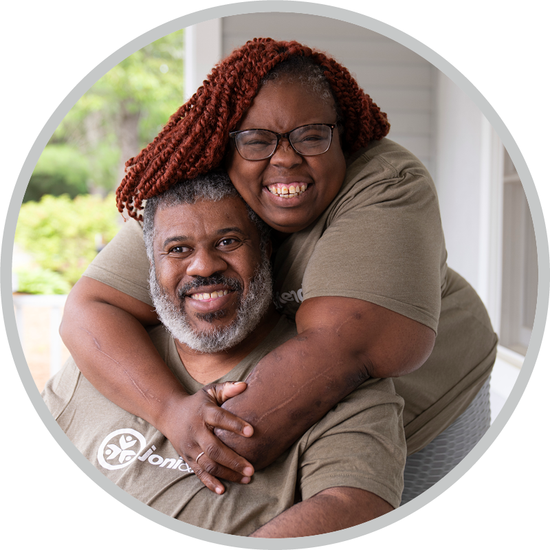 Smiling older couple embraces each other on a porch, wearing matching khaki shirts.