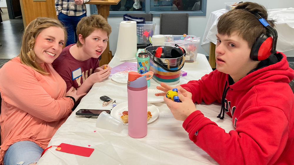 A group of people sitting at a table eating pizza and playing with sensory toys